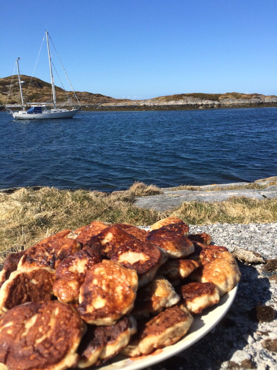 Et fat med nystekte kaker på svaberget, med en seilbåt og holmer bak